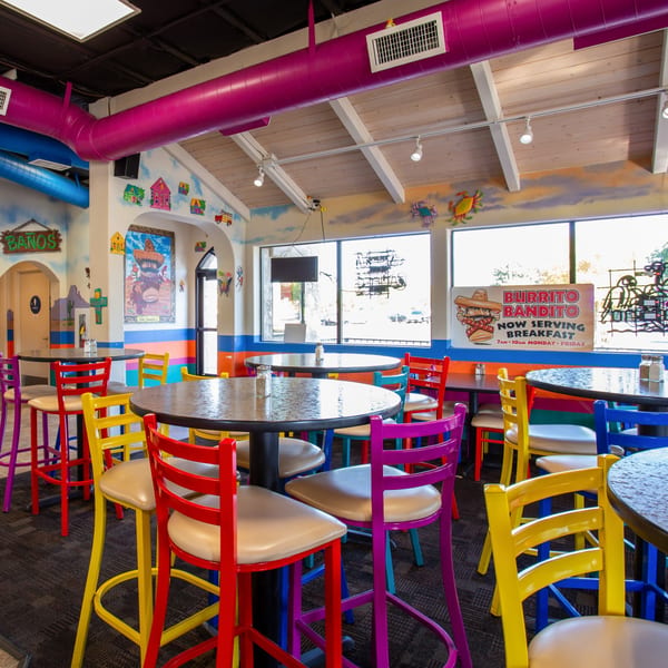 Colorful Burrito Bandito dining room with bright chairs, murals, and a breakfast sign.