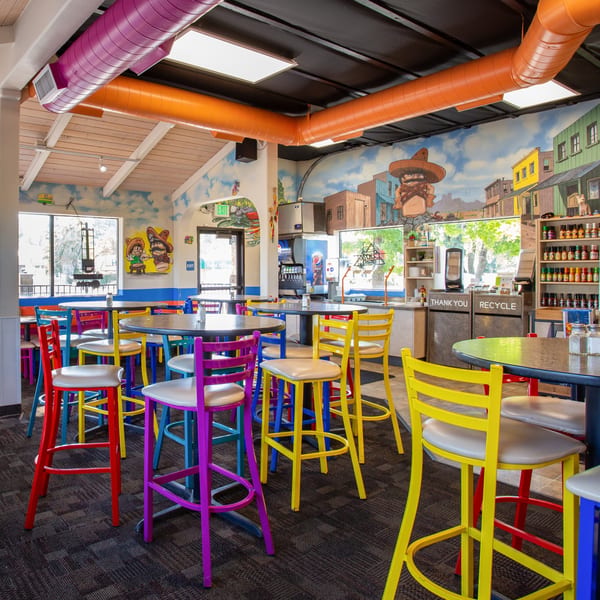 Colorful interior of Burrito Bandito with vibrant chairs, tables, and a mural depicting a desert town.