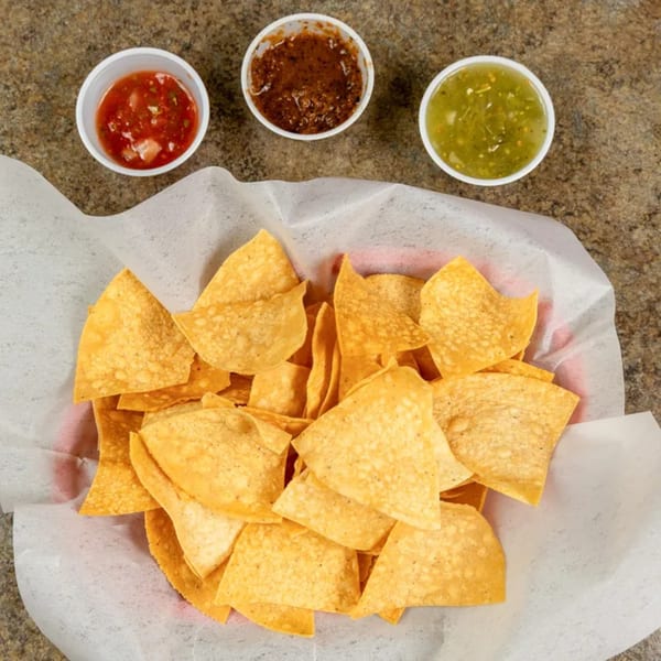 A basket of tortilla chips with three small cups of salsa: red, dark red, and green.