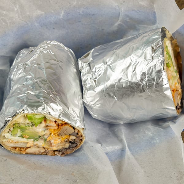 Two Burrito Bandito burritos, one partially unwrapped showing chicken, avocado, and cheese, in foil.