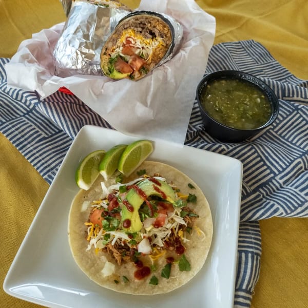 A Burrito Bandito taco and burrito with salsa verde and lime wedges on a white plate.