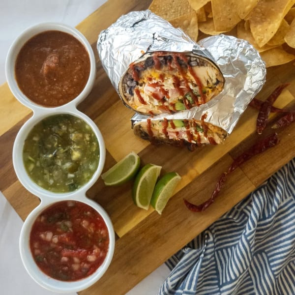Burrito Bandito's chicken burrito, cut in half, with three salsas, lime wedges, and tortilla chips.