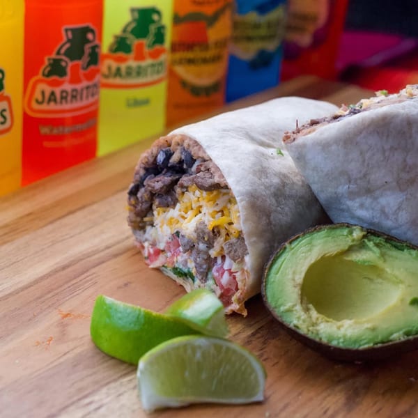 Two Burrito Bandito burritos, one cut open, with limes, avocado, and Jarritos bottles in the background.
