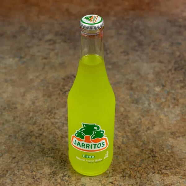 A bottle of bright green Jarritos lime soda stands upright on a textured brown surface.