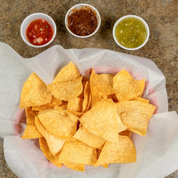 A basket of tortilla chips with three small cups of salsa: red, dark red, and green.
