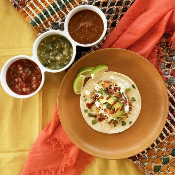 Overhead view of a Burrito Bandito taco with avocado, salsa, and lime, alongside three bowls of salsa.