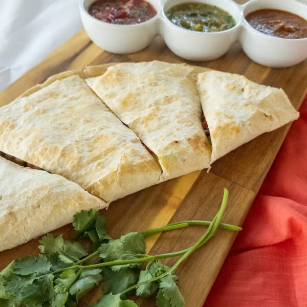 Burrito Bandito quesadilla slices with cilantro and three dipping sauces on a wooden board.