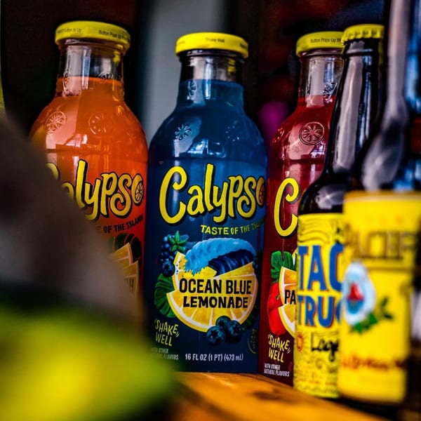 A close-up of several colorful Calypso brand lemonade bottles, including Ocean Blue, on a wooden surface.
