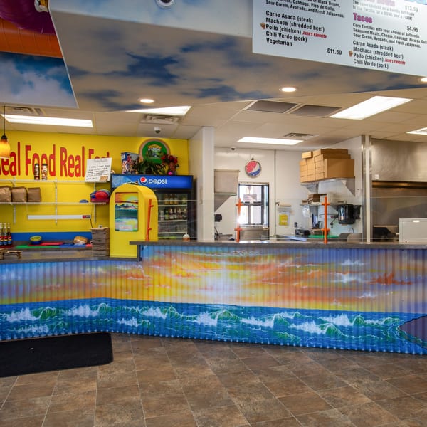 Burrito Bandito's counter with a vibrant ocean mural, menu boards, and a Pepsi cooler.