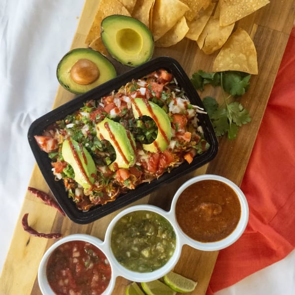 Burrito Bandito's Mexican bowl with avocado, salsa, chips, and limes on a wooden board.