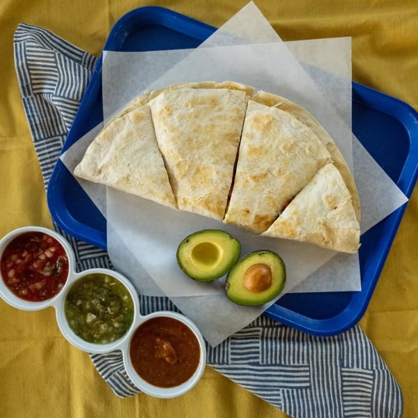 Burrito Bandito quesadilla on a blue tray with three salsas and two avocado halves.